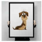 Close-up of black framed cute dachshund cartoon wall art print held by hands, showing detailed fluffy long dog illustration with expressive big eyes