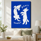 Stretched canvas wall art of two white dancing dogs on a bold cobalt blue background with "Don't Worry" text above a white sofa with sage green and cream cushions, a linen throw blanket, potted greenery, and a ceramic table lamp in a bright living room