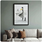 Framed watercolor art print of a woman in flowing dress with dog by the sea, hung above a neutral linen sofa on a sage green wall