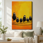Stretched canvas funny black birds on a wire wall art featuring five shaggy wide-eyed black birds of different sizes huddled together on a wire against a glowing warm amber and golden yellow oil-painted background, hung above a white sofa with sage green pillows in a bright living room