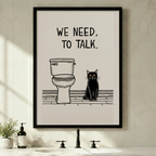 Black framed funny we need to talk black cat bathroom canvas art with bold hand-lettered we need to talk text above a minimalist line drawing of a toilet beside a serious black cat with amber eyes sitting on a wood-grain floor in a clean black and white composition on a warm off-white background, displayed above a minimalist bathroom sink with a black faucet, soap dispenser, and small potted plant