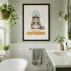 Black framed funny raccoon with towel and coffee I Can't Adult Today canvas art with a round fluffy gray raccoon in a blue towel turban holding a steaming coffee cup with a tired expression above a golden yellow I Can't Adult Today text banner on a soft off-white background, hung in a bright boho bathroom with white subway tiles gold hardware a freestanding tub and hanging plants