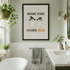 Black framed cute Halloween ghost Wash Your Hands Boo canvas wall art hung on a sage green wall above a towel bar in a bright bathroom with white subway tiles, freestanding tub, gold fixtures and hanging potted plants