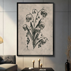 Framed gothic dark botanical skull lily of the valley canvas wall art with five human skulls replacing flower blooms on a stem with dark leaves in charcoal sketch style on aged beige background displayed on a dark grey wall in a modern living room