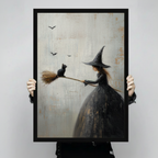 Person holding large framed gothic romantic oil painting young witch in black dress holding broomstick with black cat perched on tip and bats flying on aged cream textured background canvas print with both hands - close up view of whimsical Halloween witch and black cat broom wall art with black frame finish