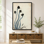 Black framed Japanese ink style black cats canvas art with four surreal black cat heads on long flowing blue-gray stems rising from grass on a vintage parchment background, displayed above a rattan storage console in a bright entryway