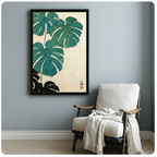 Framed Japanese monstera botanical canvas print hanging on a light blue-gray wall above a linen armchair with a draped throw blanket