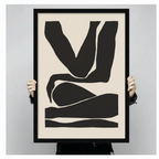 Person holding large framed minimalist abstract figure canvas print with both hands - close up view of bold black silhouette body form wall art on cream background with black frame finish