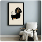 Black framed modern minimalist dachshund canvas art with a rounded flat-style black and tan wiener dog and a hand-drawn olive branch on a warm cream background, displayed on a soft blue-gray wall beside a white upholstered folding armchair draped with a cream linen throw blanket