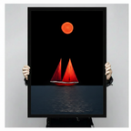 Hand-held display of a black-framed canvas art print featuring a dramatic minimalist red sailboat with twin sails beneath a glowing orange moon on a deep black ocean — bold nautical wall art