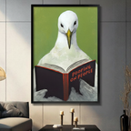 Black framed funny seagull reading Pooping on People book canvas wall art with olive green background displayed in a modern dark gray living room with charcoal sofa, black coffee table and gold candlestick holders