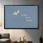 Black framed Hide Your Fries seagull funny quote canvas wall art with dusty blue background displayed in a modern dark gray living room with gray sofa, candlestick holders and tall black vase