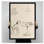 Person holding a black framed funny pencil sketch long-nosed dachshund reaching for croissant and coffee on cafe table art print on cream background against a light gray backdrop