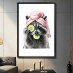 Pencil sketch raccoon with a pink towel turban and cucumber slices in a black frame, hung on a dark grey wall above a console table with candle holders in a modern living room