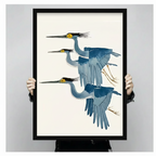 Hands holding large framed three flying herons canvas print - full artwork detail of Japanese ukiyo-e watercolor painting with three graceful herons in layered flight formation blue grey gradient feathers bold yellow eyes black crest plumes and golden talon legs on clean cream background