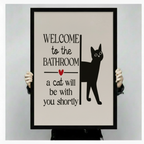 Hands holding large framed Welcome to the Bathroom black cat canvas print - full artwork detail of humorous cat typography with bold serif font red heart and black cat silhouette on cream background