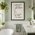 Black-framed funny cat bathroom art print with handwritten-style quote, hung in a bright white subway tile bathroom with hanging plants, dual vanity, and gold hardware