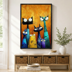 Black framed whimsical colorful cat family canvas art with five quirky cats in black teal blue yellow and purple with oversized googly eyes and expressive faces rendered in bold impasto brushstrokes on a vibrant golden amber floral-textured background, displayed above a rattan storage console in a bright entryway