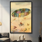 Framed whimsical watercolor illustration canvas wall art of an old man riding a bicycle suspended from a colorful patchwork parachute soaring through a warm golden sky surrounded by multicolored flying birds on a dark grey wall in a modern living room