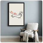 Minimalist wiener dog Oui-Ner canvas art in black frame hung on blue-grey wall beside white linen armchair in Scandinavian-style room