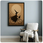 Black framed witch and cat bicycle print on grey wall beside armchair, moody vintage halloween wall decor