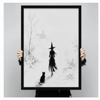 Person holding a black framed canvas print of a witch and black cat in a misty winter landscape, showing actual print size against a neutral background