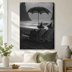 Gallery wrap canvas of two witches in pointed hats lounging under a lace umbrella on a moody beach with glowing-eyed black cat, hung above a white sofa in a bright living room