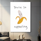 Unframed canvas wall art of smiling peeled banana with "You're So Appealing" pun text, large format display on grey wall with candles